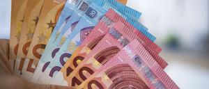 Eine Frau hält Banknoten von 10, 20 und 50 Euro gefächert in der Hand.