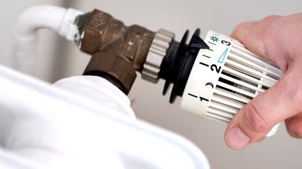  Eine Frau dreht am Thermostat eines Heizkörpers.