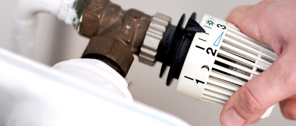  Eine Frau dreht am Thermostat eines Heizkörpers.