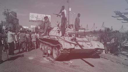 Unterstützer der sudanesischen Armee auf einem ausgebrannten Panzer der RSF-Miliz.