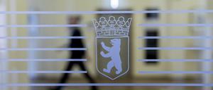 Das Wappen von Berlin ist im Roten Rathaus auf einer Glastür zu sehen, während dahinter eine Person vorbeigeht.