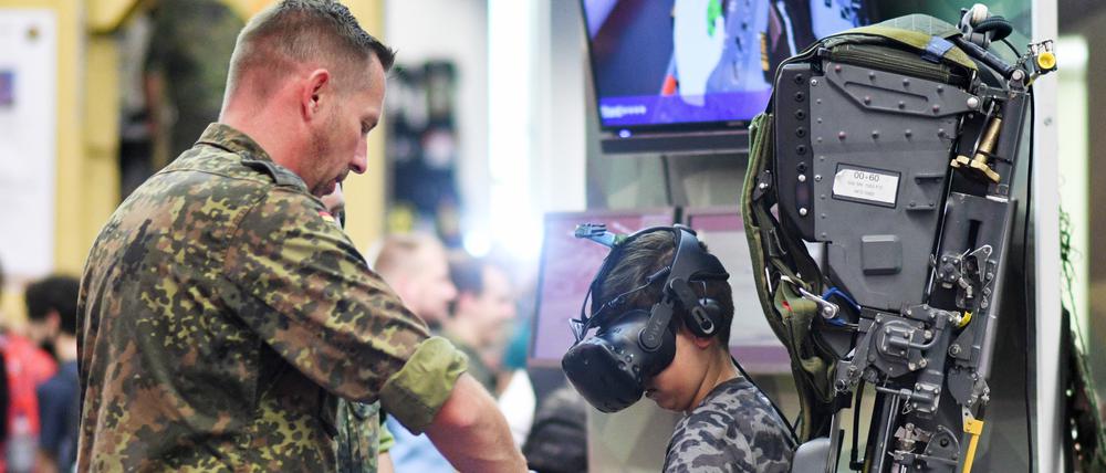 Ein Junge sitzt bei einer Computerspielemesse auf dem Stand der Bundeswehr auf dem Sitz eines Tornado und wird von einem Soldaten angeleitet.