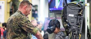 Ein Junge sitzt bei einer Computerspielemesse auf dem Stand der Bundeswehr auf dem Sitz eines Tornado und wird von einem Soldaten angeleitet. 