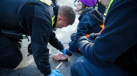 28.04.2023, Berlin: Ein Polizeibeamter löst die Hand einer Klimaaktivistin von der Straße am Großen Stern vor der Siegessäule. Hier haben sich zuvor Aktivisten der Klimabewegung Letzte Generation auf die Fahrbahn gesetzt und die Hand auf den Asphalt geklebt. Foto: Kay Nietfeld/dpa +++ dpa-Bildfunk +++