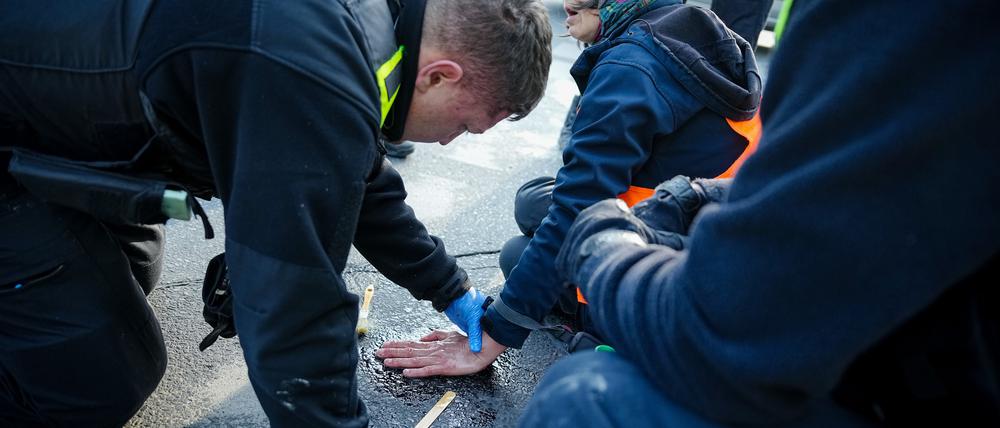 28.04.2023, Berlin: Ein Polizeibeamter löst die Hand einer Klimaaktivistin von der Straße am Großen Stern vor der Siegessäule. Hier haben sich zuvor Aktivisten der Klimabewegung Letzte Generation auf die Fahrbahn gesetzt und die Hand auf den Asphalt geklebt. Foto: Kay Nietfeld/dpa +++ dpa-Bildfunk +++