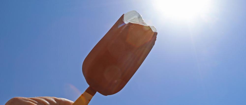 Die Sonne strahlt am Mittag vom blauen wolkenlosen Himmel. Davor ein Eis am Stiel mit Schokolade (Archivbild).