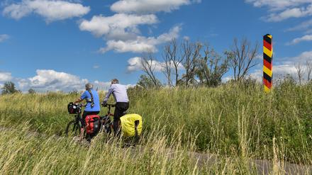 Radwandertouristen fahren mit ihren bepackten Fahrrädern auf dem Oder-Neiße-Radweg, der sich im Oderbruch auf dem Deich am deutsch-polnischen Grenzfluss Oder nahe Reitwein (Brandenburg) befindet.