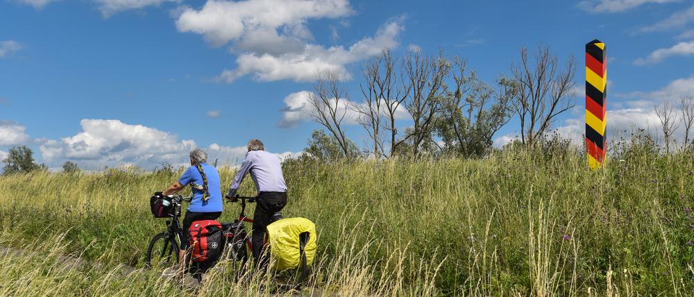 Radwandertouristen fahren mit ihren bepackten Fahrrädern auf dem Oder-Neiße-Radweg, der sich im Oderbruch auf dem Deich am deutsch-polnischen Grenzfluss Oder nahe Reitwein (Brandenburg) befindet.
