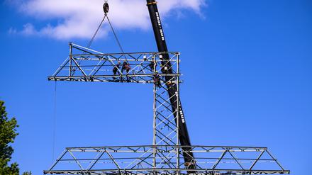 Monteure bauen einen Strommast auseinander, dann werden einzelne Teile per Kran zu Boden gelassen.