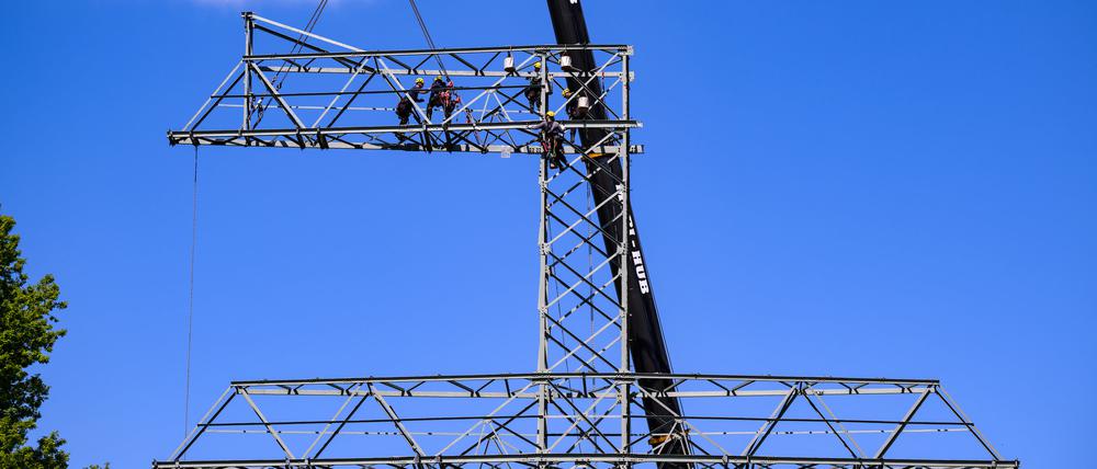 Monteure bauen einen Strommast auseinander, dann werden einzelne Teile per Kran zu Boden gelassen.