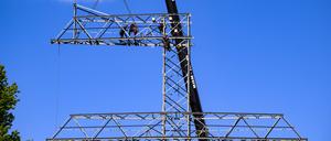 Monteure bauen einen Strommast auseinander, dann werden einzelne Teile per Kran zu Boden gelassen.
