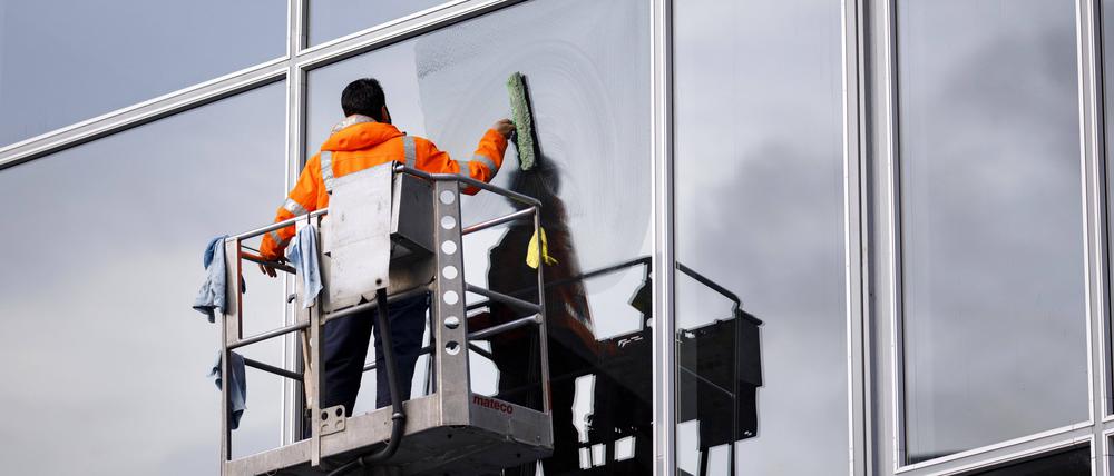 Ein Fensterputzer reinigt auf einer Hebebühne die Scheiben der Eingangshalle des Kölner Hauptbahnhofs.