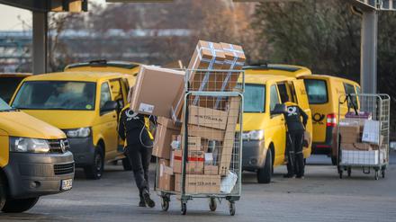 Eine Mitarbeiterin der Deutsche Post DHL zieht einen vollen Paketwagen zu ihren Fahrzeug über den Hof eines Zustellpunktes. 