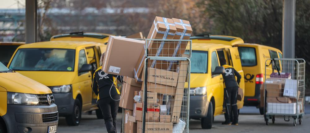 Eine Mitarbeiterin der Deutsche Post DHL zieht einen vollen Paketwagen zu ihren Fahrzeug über den Hof eines Zustellpunktes. 