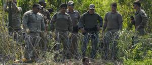 Texanische Polizisten stehen hinter einer Barriere am Ufer des Rio Grande, während eine Migrantin auf der mexikanischen Seite weint. 