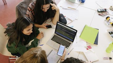 A high school study group working together on a project, using a smartphone and laptop together.