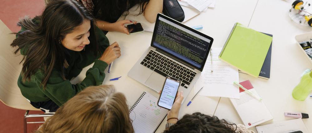 A high school study group working together on a project, using a smartphone and laptop together.