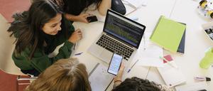 A high school study group working together on a project, using a smartphone and laptop together.