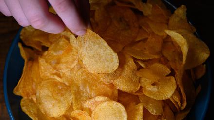 Die Hand eines Jungen greift in eine Schüssel mit Kartoffelchips.