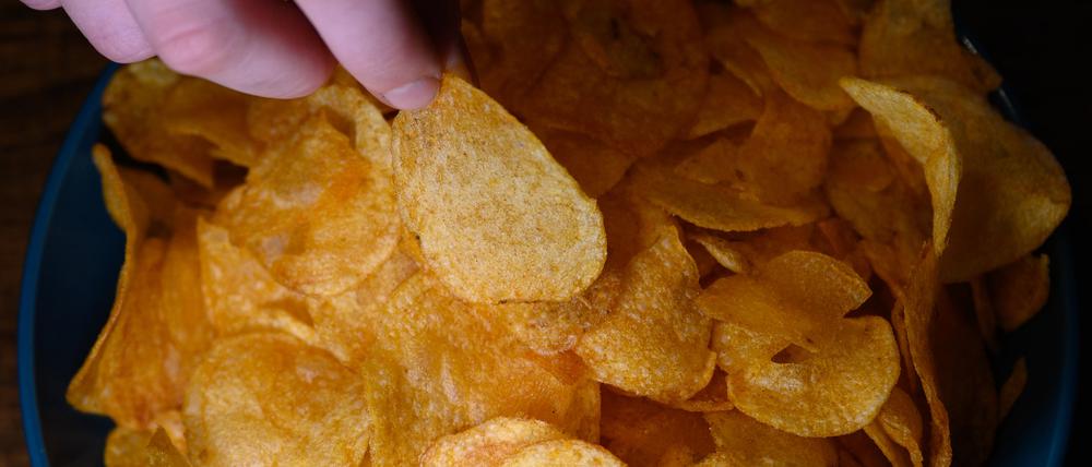 Die Hand eines Jungen greift in eine Schüssel mit Kartoffelchips.