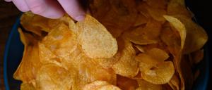Die Hand eines Jungen greift in eine Schüssel mit Kartoffelchips.