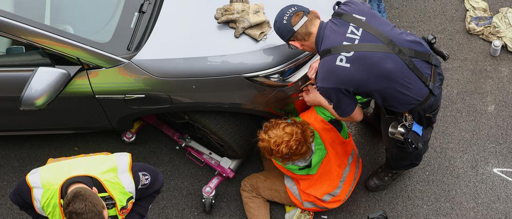 Ja, wo kleben sie denn? Polizisten lösen einen Aktivisten der „Letzten Generation“ von einem Fahrzeug auf der Stadtautobahn A100 ab.