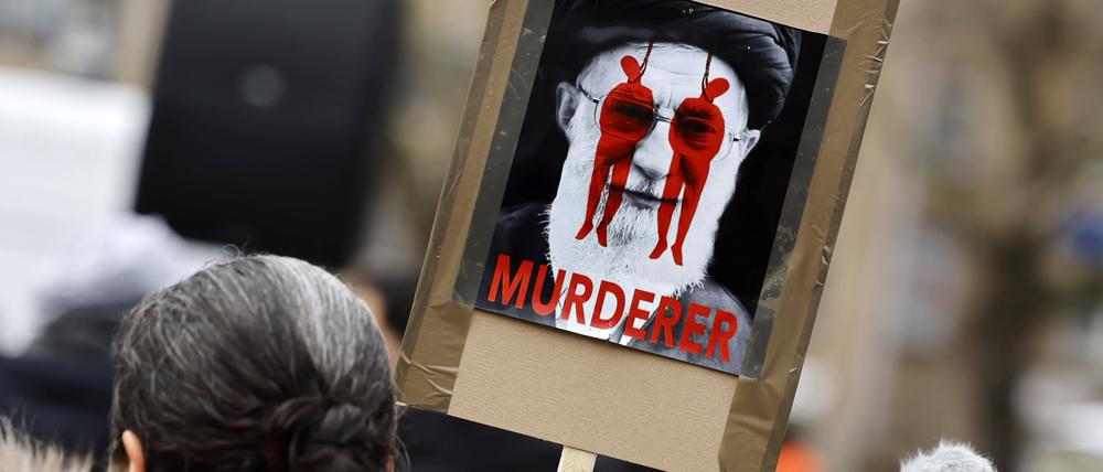 Menschen nehmen an einer Kundgebung gegen das iranische Regime auf dem Neumarkt in Köln teil. Ein Plakat zeigt Ali Chamenei als Mörder.