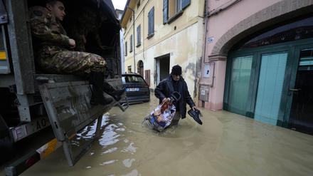17.05.2023, Italien, Castel Bolognese: Ein Anwohner geht an einem Armeelastwagen in einem überschwemmten Dorf vorbei.