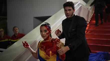 Die Frau, gekleidet in ukrainischen Farben, die mit einer roten Substanz beschmiert ist, wird bei der Premiere des Films „Acide“ bei den 76. Internationalen Filmfestspielen vom Sicherheitspersonal abgeführt. 
