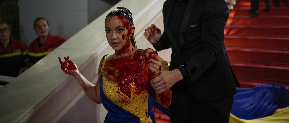 Die Frau, gekleidet in ukrainischen Farben, die mit einer roten Substanz beschmiert ist, wird bei der Premiere des Films „Acide“ bei den 76. Internationalen Filmfestspielen vom Sicherheitspersonal abgeführt. 