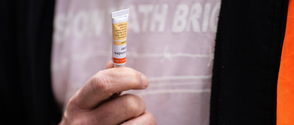 Ein Mitglied der „Letzten Generation“ hält eine Tube Sekundenkleber in der Hand.