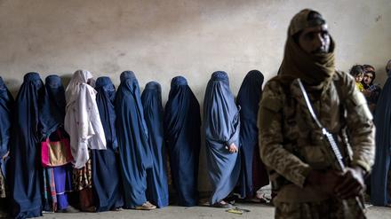 Ein Taliban-Kämpfer steht Wache, während Frauen bei der Lebensmittelverteilung warten.