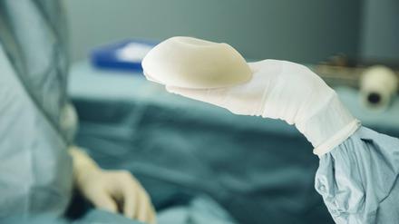 Hand hält Brustimplantat während Operation.