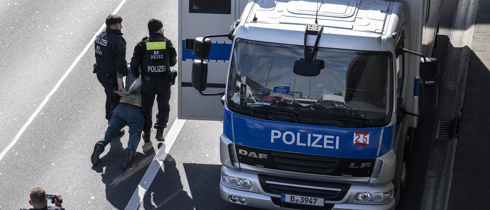 Zwei Polizisten tragen einen Klimaaktivisten zum Gefangenentransport auf der A100.