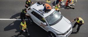 Polizisten schieben einen Wagen bei einer Blockade der Letzten Generation auf der Autobahn 100 auf den Standstreifen.