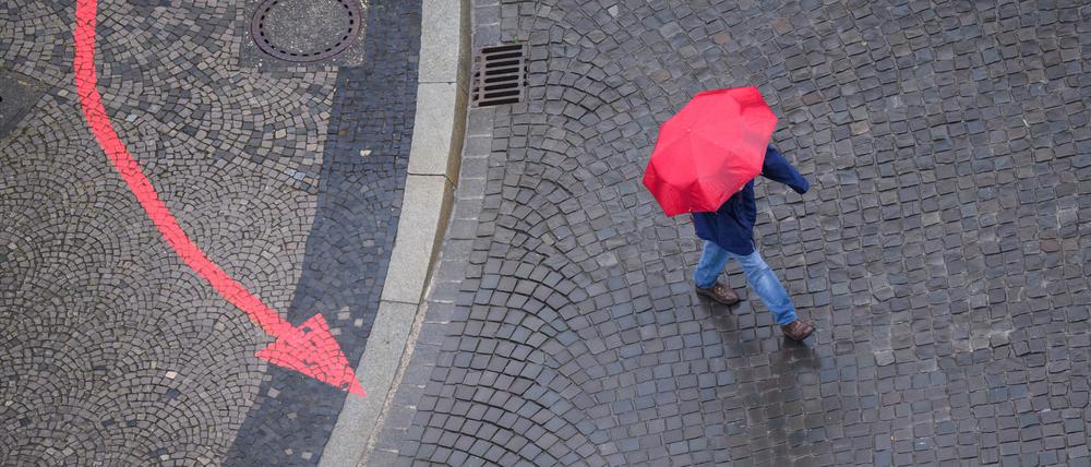 Niedersachsen, Hannover: Ein Mann geht mit einem roten Regenschirm am Neuen Rathaus vorbei.