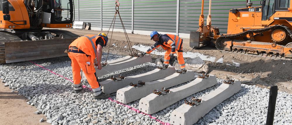 Arbeiter verlegen mit Hilfe eines Raupenbaggers Betonschwellen.