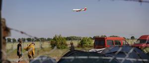 Teilnehmer am Protestcamp bauen ihre Zelte auf, während über ihnen ein Flugzeug fliegt. 