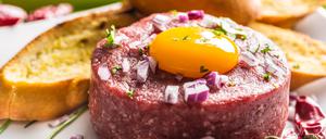 Beef tartare with egg yolk red onion chili peppers herbs and bruschetta.