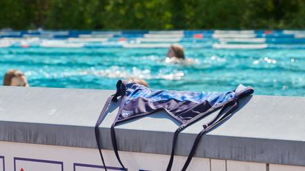 Ein Badeanzug liegt auf einer Mauer im Prinzenbad, dahinter schwimmen Menschen im Becken ihre Bahnen.