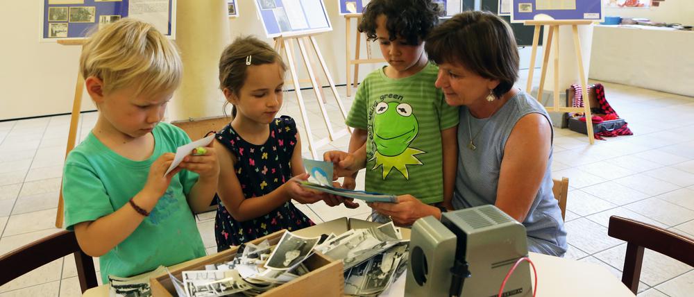 Kita-Leiterin Irmgard Wienecke zeigt Levi, Hannah und Emilia alte Fotos der Einrichtung.