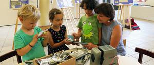 Kita-Leiterin Irmgard Wienecke zeigt Levi, Hannah und Emilia alte Fotos der Einrichtung.