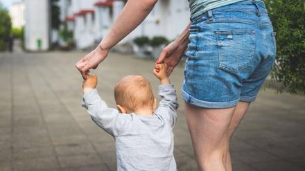 Eine Frau hält ein Kleinkind an den Händen und führt es eine Straße entlang. 