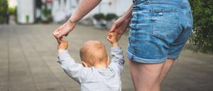 Eine Frau hält ein Kleinkind an den Händen und führt es eine Straße entlang. 