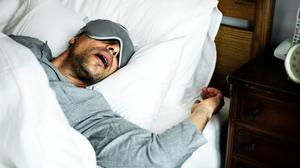 Ein schlafender Mann liegt im Bett und ringt mit offenem Mund um Luft.