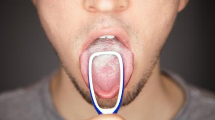 Ein Mann reinigt seine Zunge mit einer Zungenbürste.