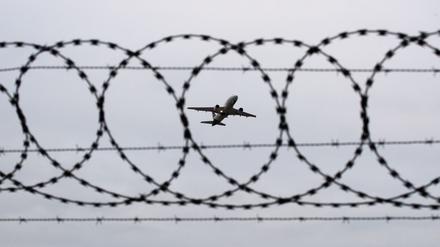 Ein Flugzeug startet am Flughafen Hannover, fotografiert durch Stacheldraht am Flughafenzaun.