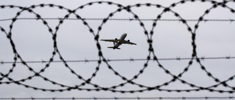 Ein Flugzeug startet am Flughafen Hannover, fotografiert durch Stacheldraht am Flughafenzaun.