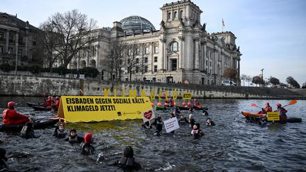 Aktivisten von verdi, AWO, dem Paritätischen und Greenpeace schwimmen und paddeln in der Spree. Sie zeigen Plakate mit der Aufschrift «Klimageld Jetzt!» und «Eisbaden gegen soziale Kälte - Klimageld jetzt!». Demonstriert wird für eine schnelle Einführung des Klimagelds.
