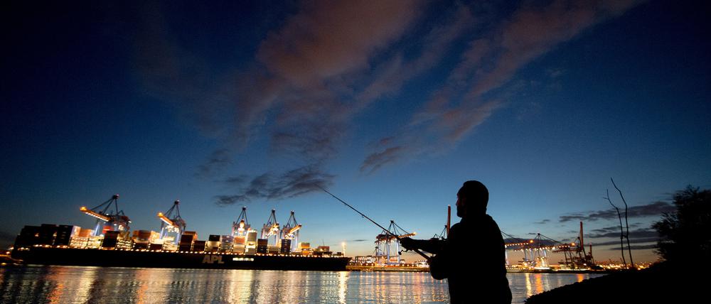Ein Mann wirft  in der Abenddämmerung am Containerterminal Altenwerder im Hamburger Hafen seine Angel aus.